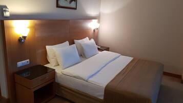 A hotel room with a wooden headboard, a bed with white linens, two bedside lamps, a nightstand with a phone and a lamp, and a wall-mounted picture.