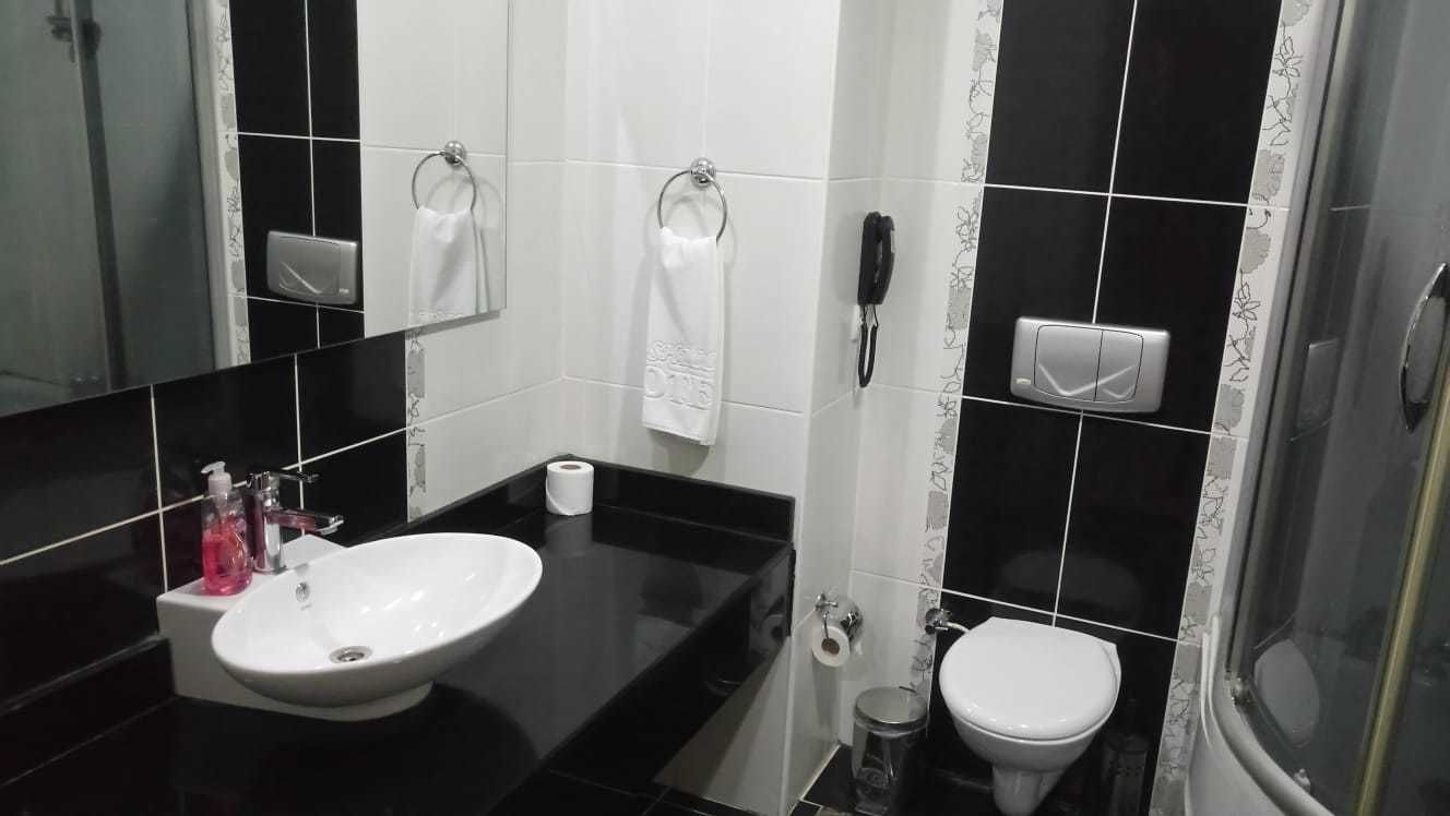 Une salle de bain moderne avec un comptoir noir, un lavabo blanc et des toilettes. On y trouve deux porte-serviettes, un sèche-mains et une poubelle.