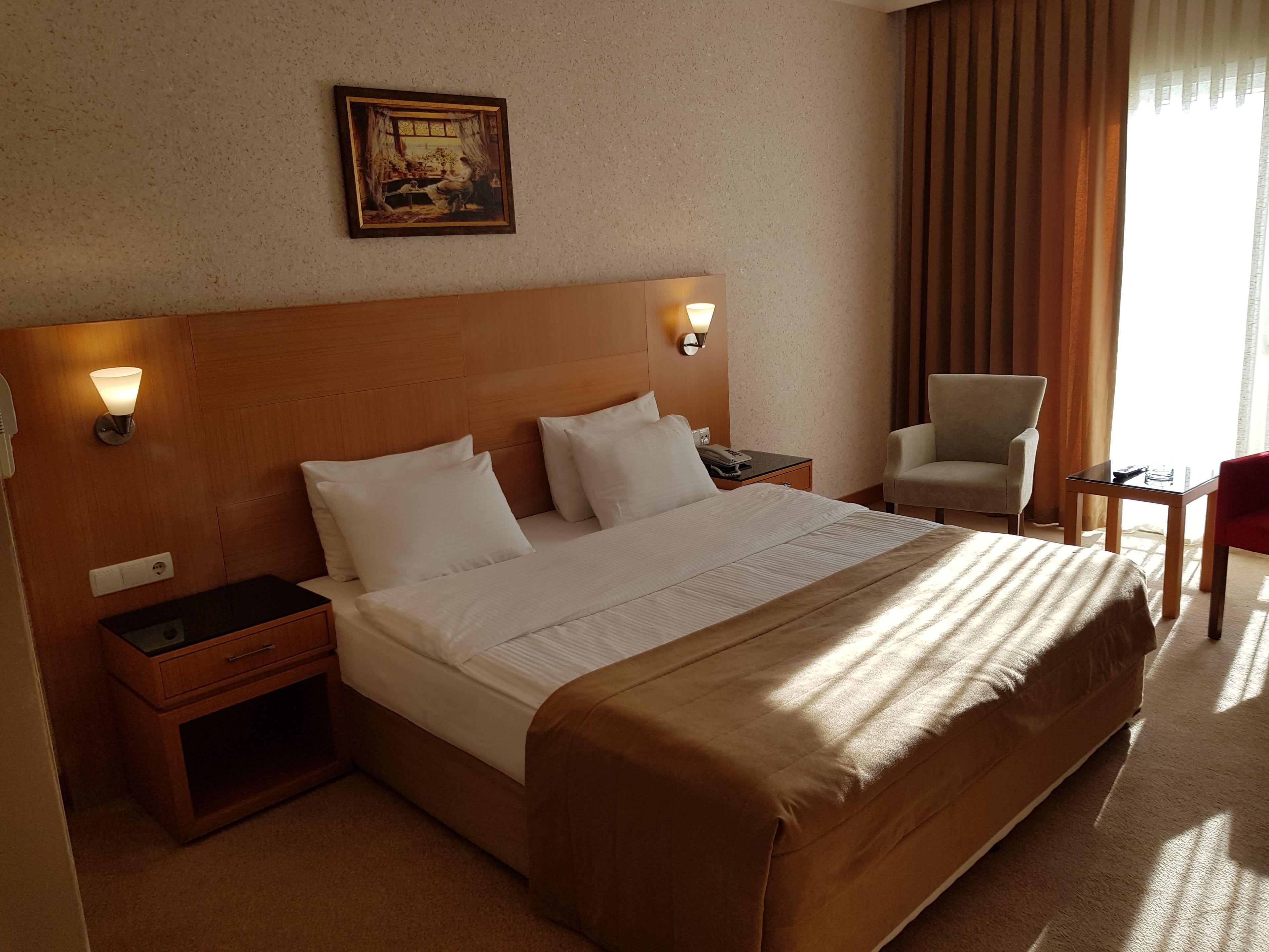 A hotel room with a large bed, bedside tables, a chair, and a desk.