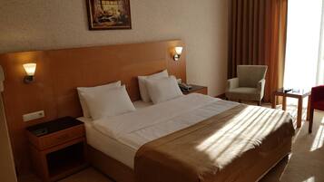 A hotel room with a large bed, bedside tables, a chair, and a desk.