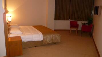 A hotel room with a bed, a desk, a chair, and a window with curtains.