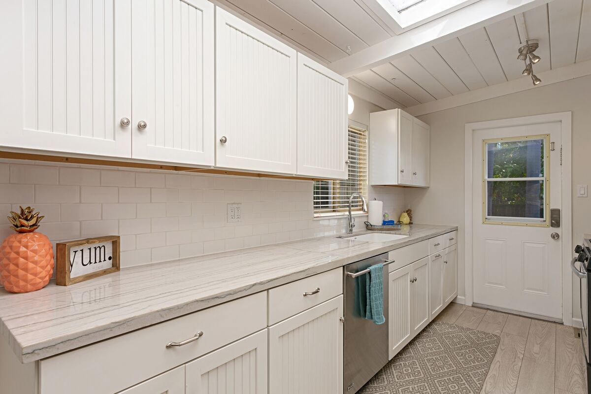 A kitchen with white cabinetry, a marble countertop, and a window with blinds.