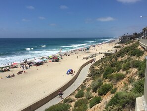 Une plage avec une promenade sinueuse, des parasols et des personnes se prélassant au soleil.