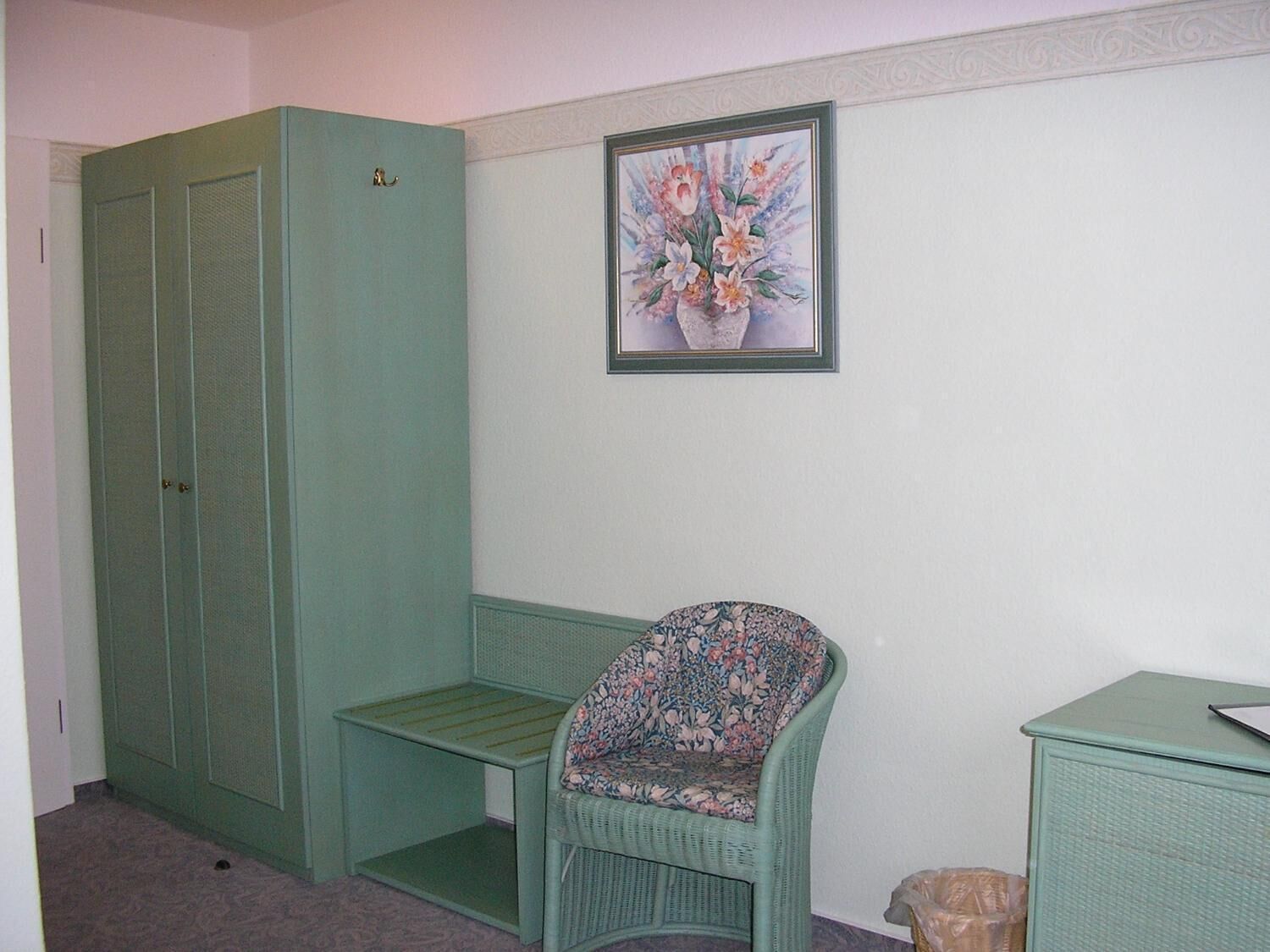 A room with a green wardrobe, a floral chair, and a small table.