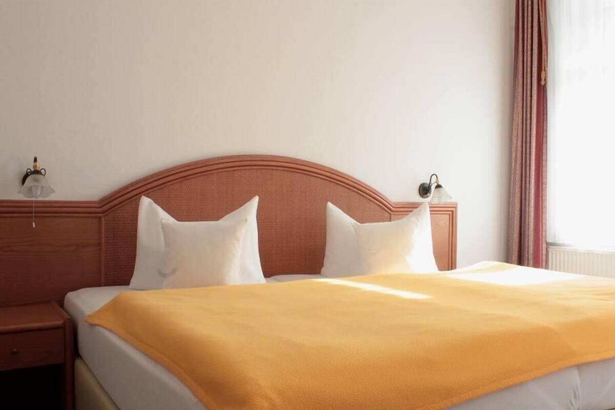 Quarto de hotel com uma cama, duas mesas de cabeceira e uma janela com cortinas.