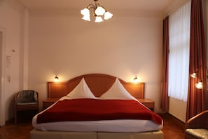 A hotel room with a large bed, two bedside lamps, a chair, and a chandelier.