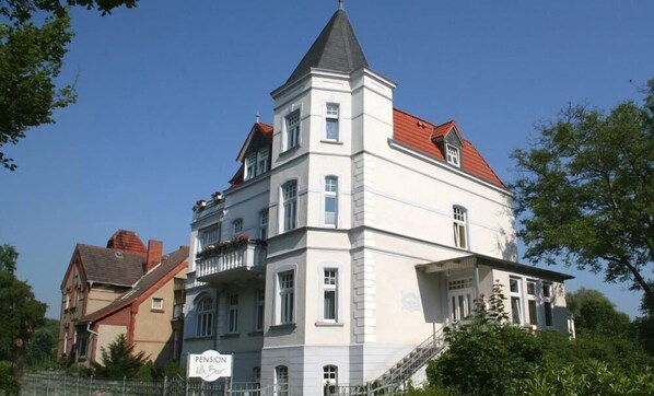 A multi-story building with a prominent corner tower, a sign reading "Pension Villa Beer," and a staircase leading to the entrance.