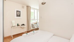Et hotelværelse med seng, skrivebord med computer, stol og vindue med gardiner.