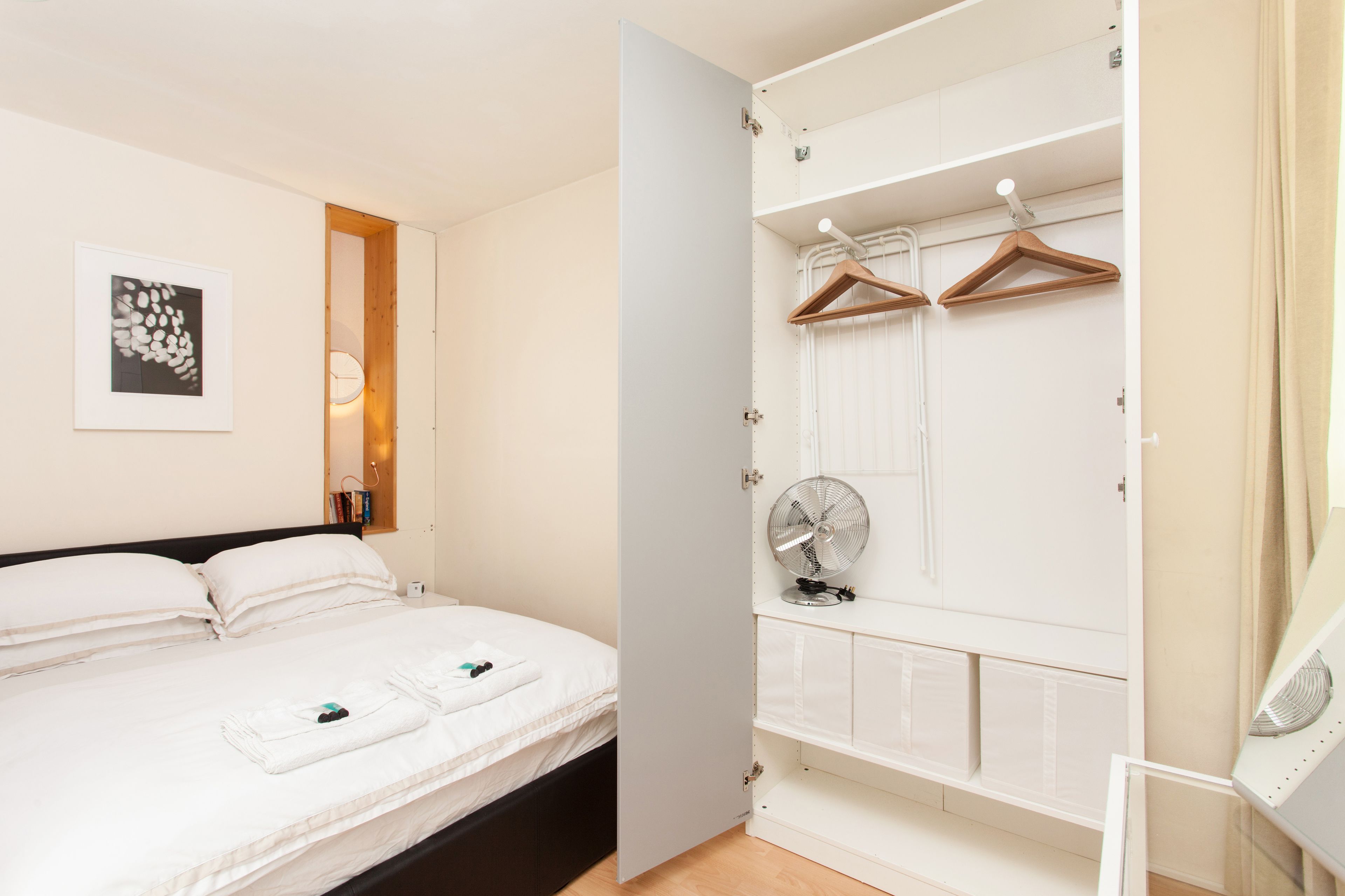 A neatly organized bedroom with a bed, bedside table, and a wardrobe with hanging space.