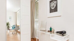 Et moderne værelse med et hvidt skrivebord, en bærbar computer, en hårtørrer og et billede af en tulipan i ramme på væggen.