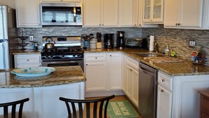 A kitchen with white cabinets, a stainless steel refrigerator, a microwave, a stove, a dishwasher, and a granite countertop. There are two chairs and a green mat on the floor. - Beach Across The Street! Great Views & Location! Sleeps 10 (Wildwood)
