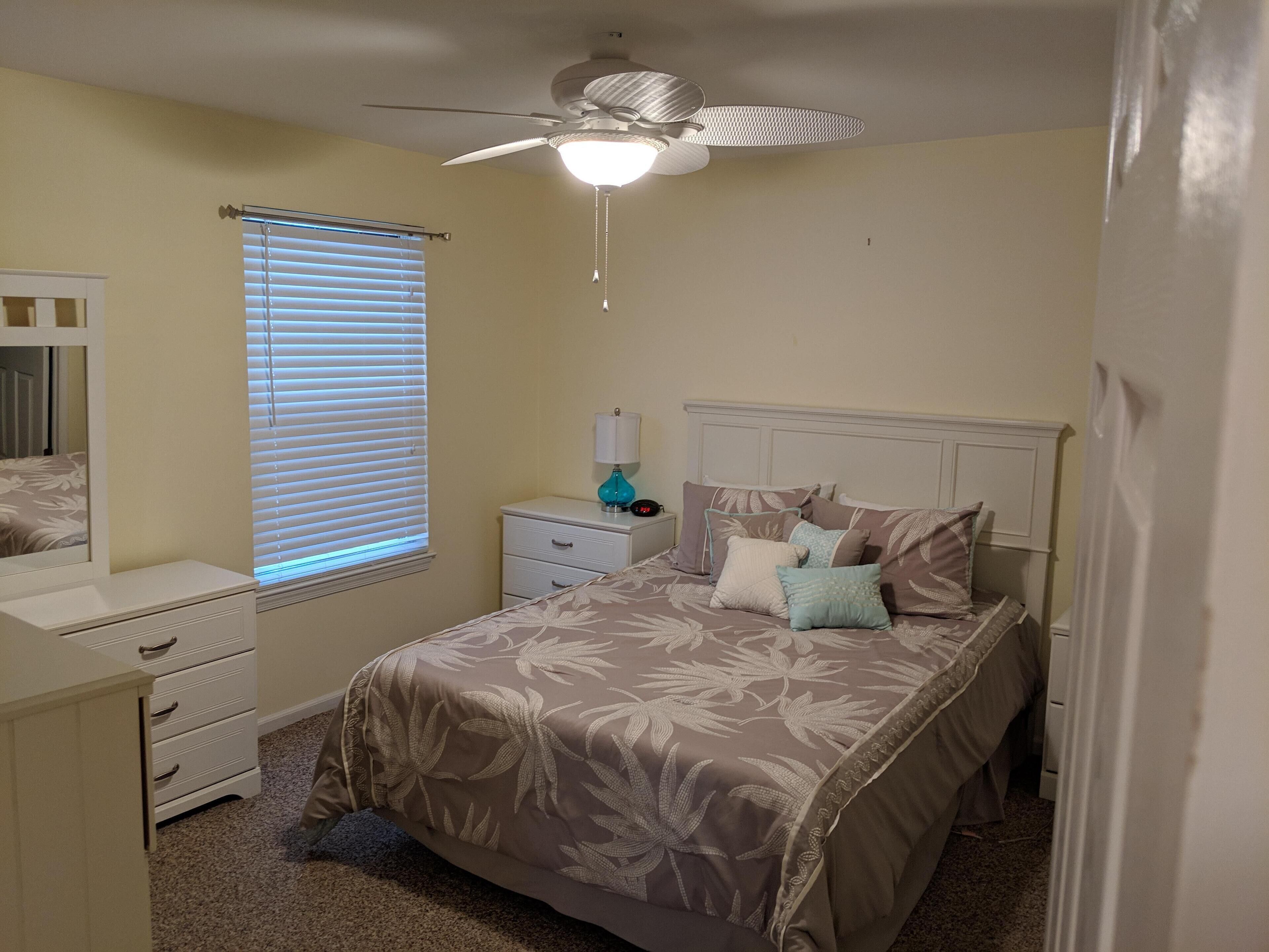A bedroom with a bed, nightstands, a dresser, a ceiling fan, and a window with blinds.