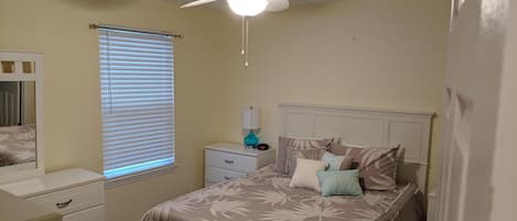 A bedroom with a bed, nightstands, a dresser, a ceiling fan, and a window with blinds.