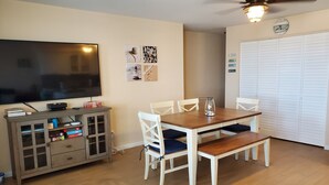 A dining area with a wooden table and chairs, a television, a cabinet with storage, and a ceiling fan. - Beach Across The Street! Great Views & Location! Sleeps 10 (Wildwood)