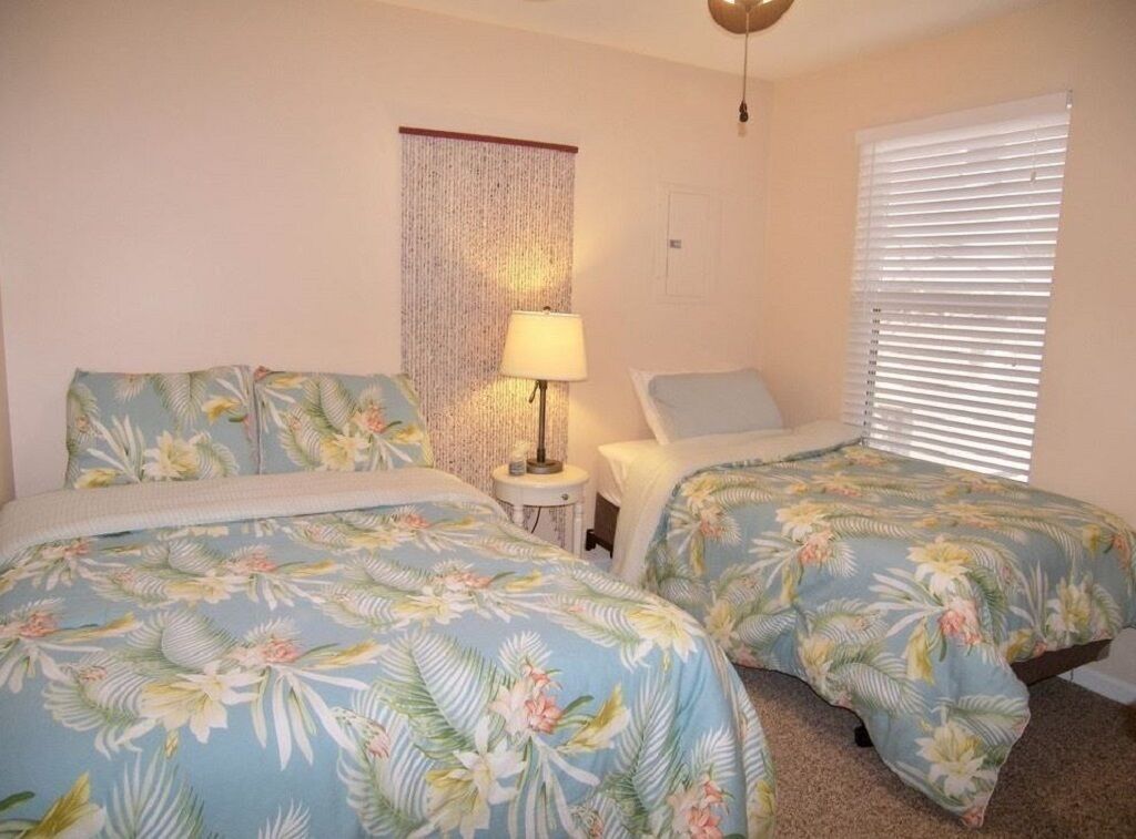 Un dormitorio con dos camas, cada una con ropa de cama floral, una lámpara de noche y una cortina.