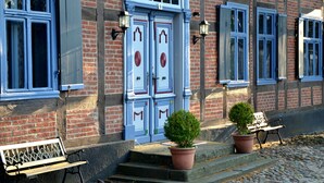 A building with a brick facade, two blue doors with decorative elements, and a bench outside. - Kulturhof (Lenzen)