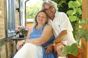 A couple sitting on a porch with a brick wall and a window.