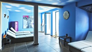A modern room with a blue wall, a large window, a bed, a clock, and a door leading to another room. - Kulturhof (Lenzen)