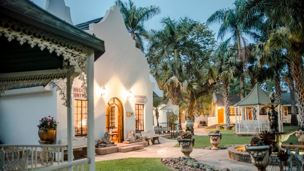 A courtyard with a white building, palm trees, and outdoor seating. - Loskop Valley Lodge and Restaurant (Groblersdal)