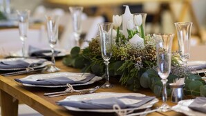 A dining table set with plates, cutlery, and glasses, surrounded by greenery and white flowers. - Loskop Valley Lodge and Restaurant (Groblersdal)