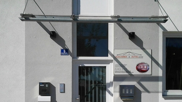 L’entrée d’un hôtel, avec un portail en métal, un panneau bleu indiquant une place de stationnement réservée aux personnes handicapées et deux plantes en pot.