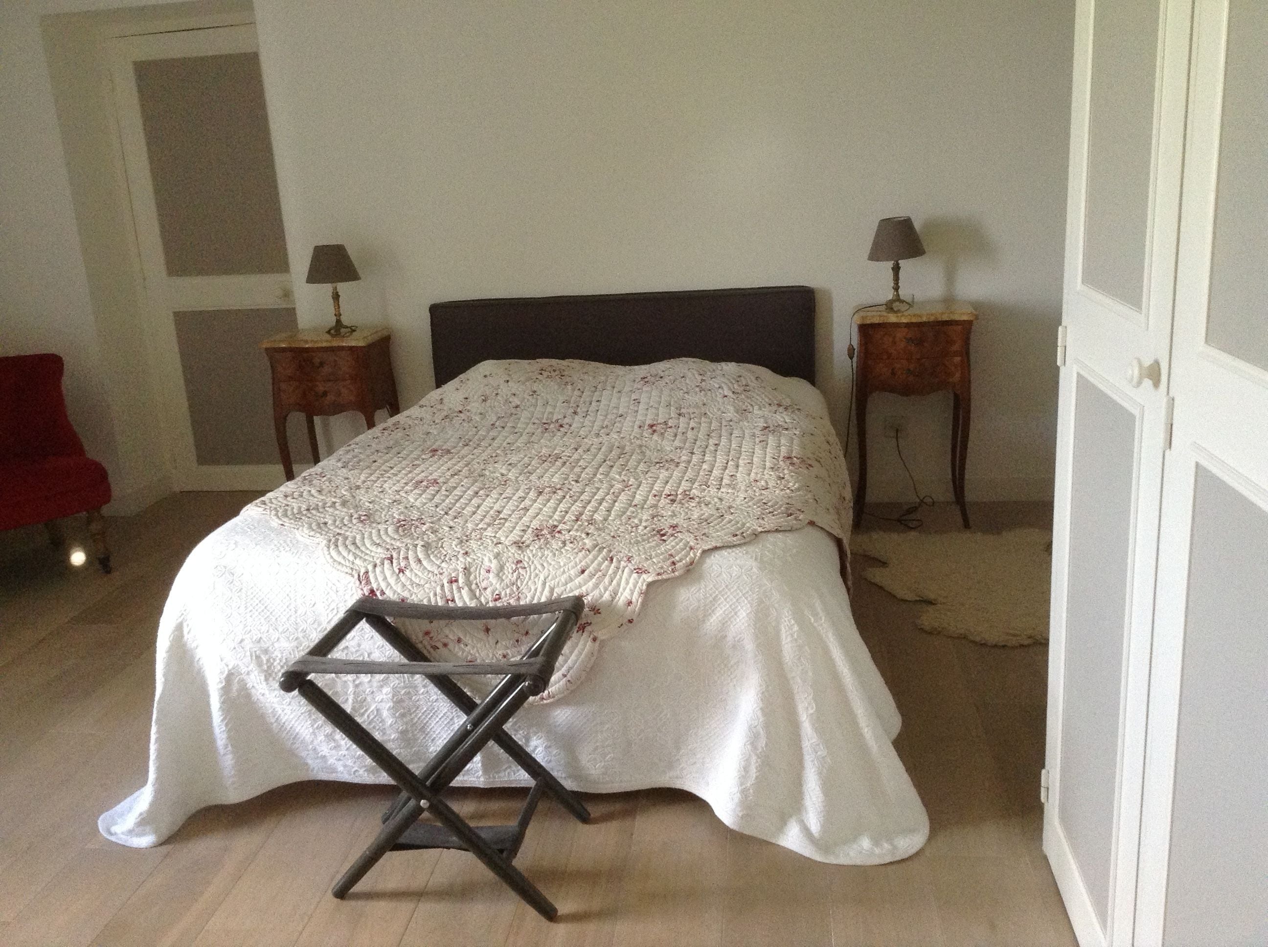 Una camera da letto con un letto, una poltrona rossa, due comodini con lampade e una porta.