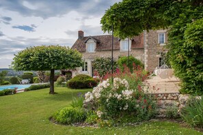 Une maison en pierre avec un jardin, une piscine et du mobilier d’extérieur.