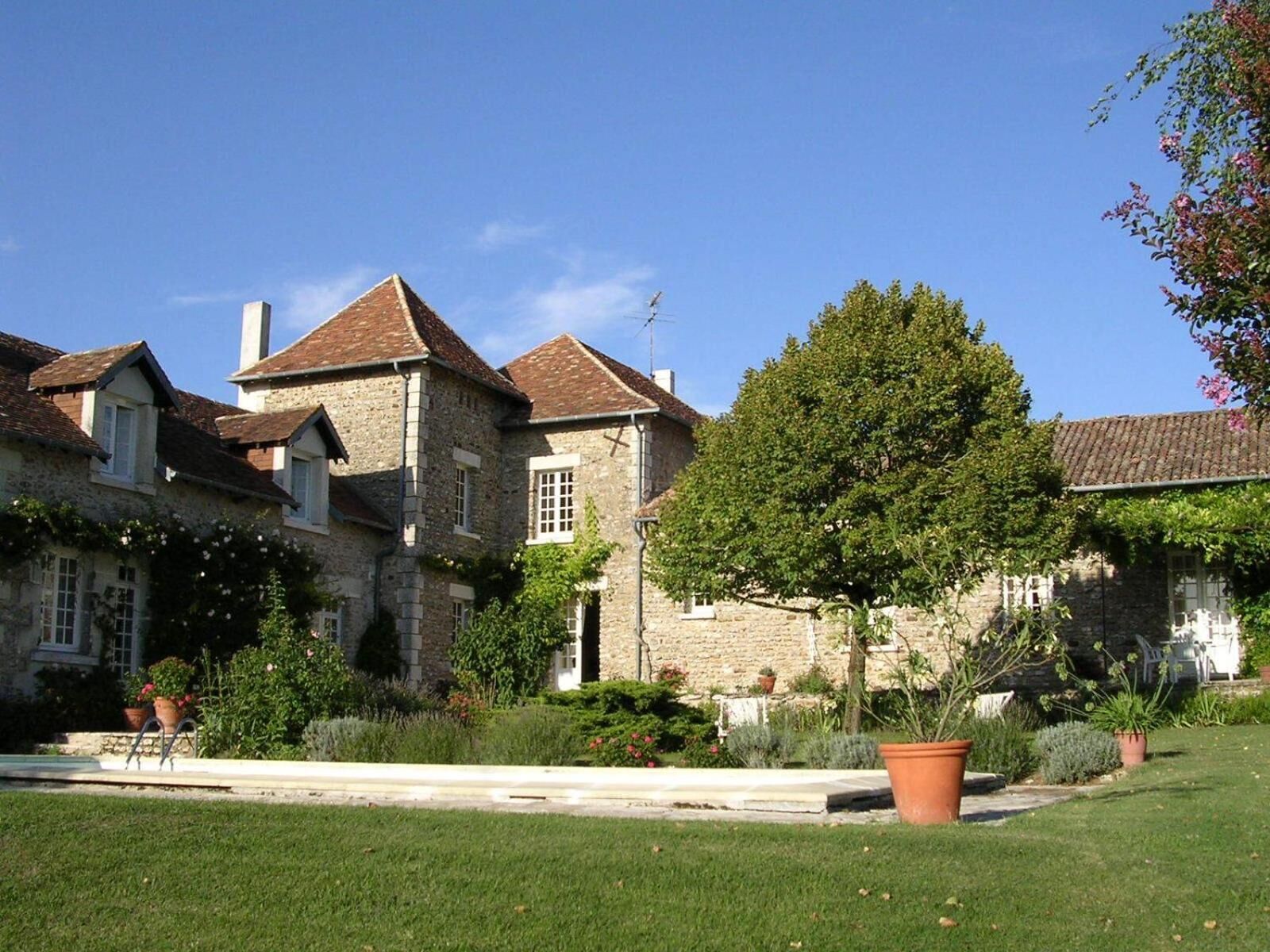 Un bâtiment en pierre avec un toit en tuiles, entouré d’un jardin bien entretenu et d’une piscine.