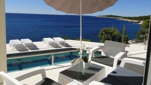 A poolside area with lounge chairs and an umbrella, overlooking a clear blue sea and a rocky coastline. - Holiday apartment with pool use and sea view (Primošten)