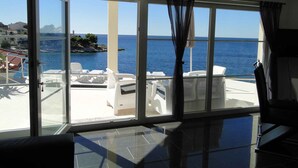 A room with large windows overlooking a coastal area with a pool and lounge chairs. - Holiday apartment with pool use and sea view (Primošten)
