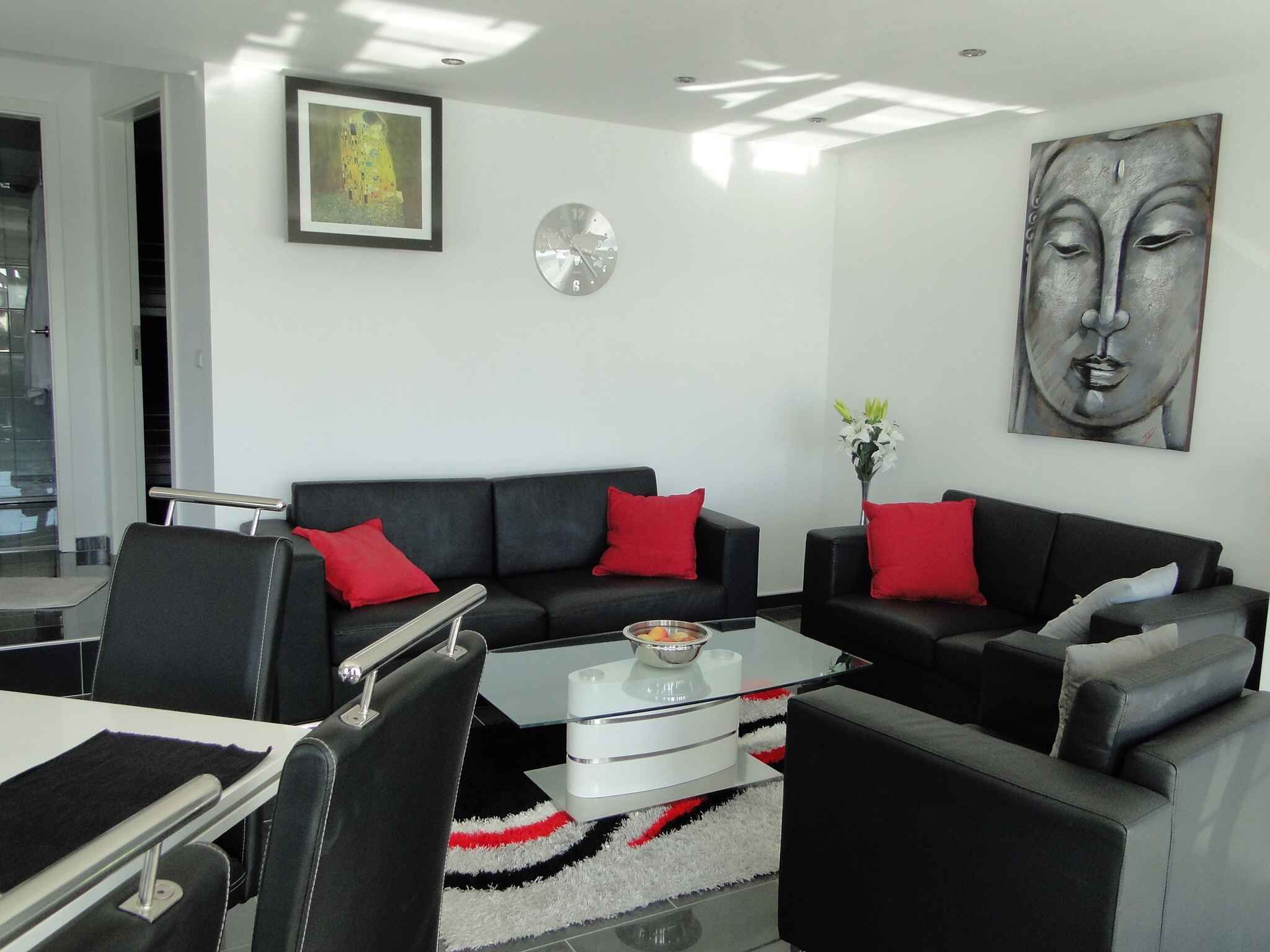 Un salon moderne avec un ensemble de canapés noirs, des coussins rouges, une table basse en verre et un tableau accroché au mur.