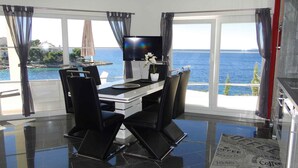 A modern dining area with a view of the sea, a flat-screen TV, and a small table with a potted plant. - Holiday apartment with pool use and sea view (Primošten)