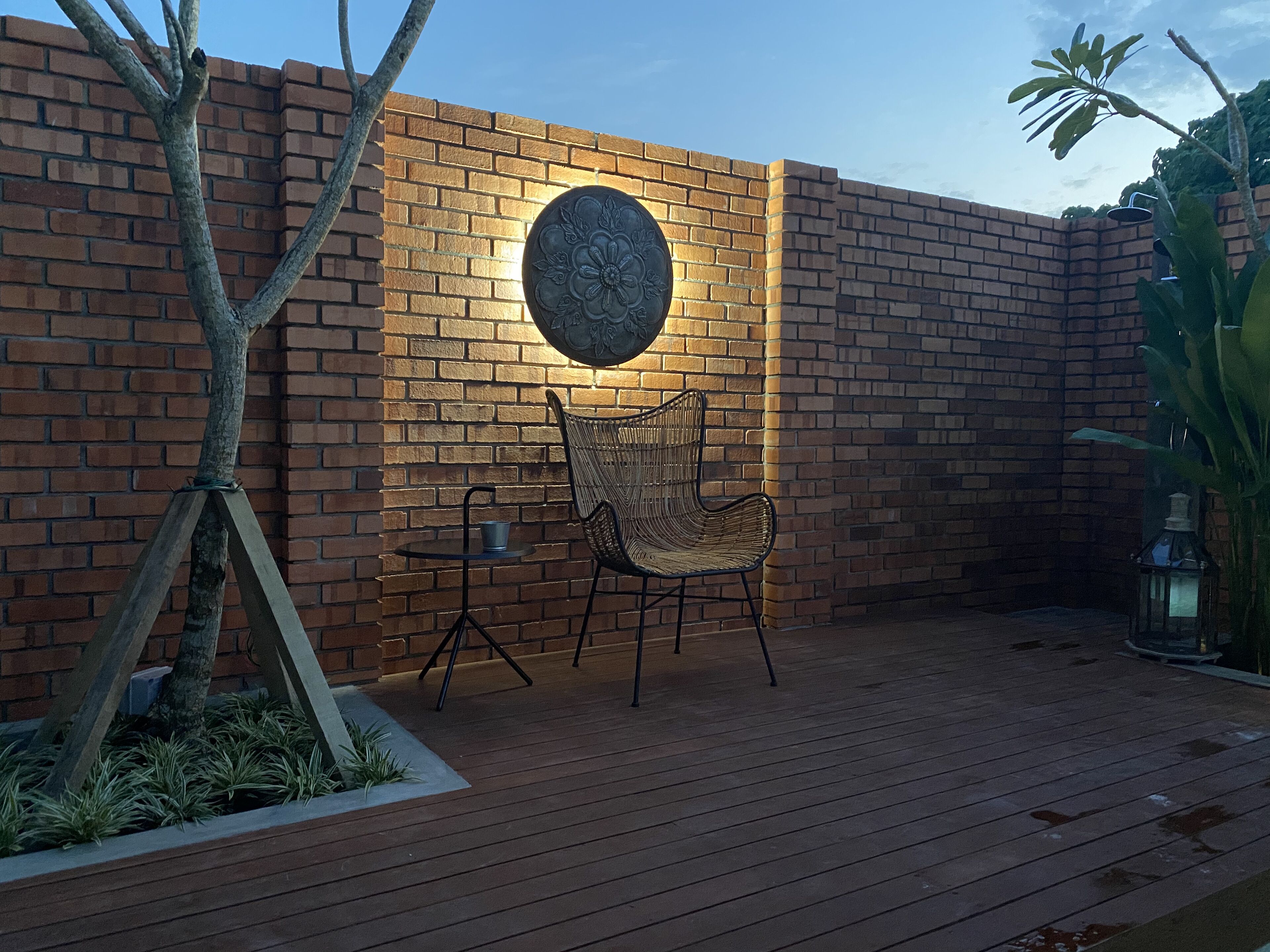 Une terrasse avec un mur en briques, un élément décoratif rond, une chaise en osier et une petite table.