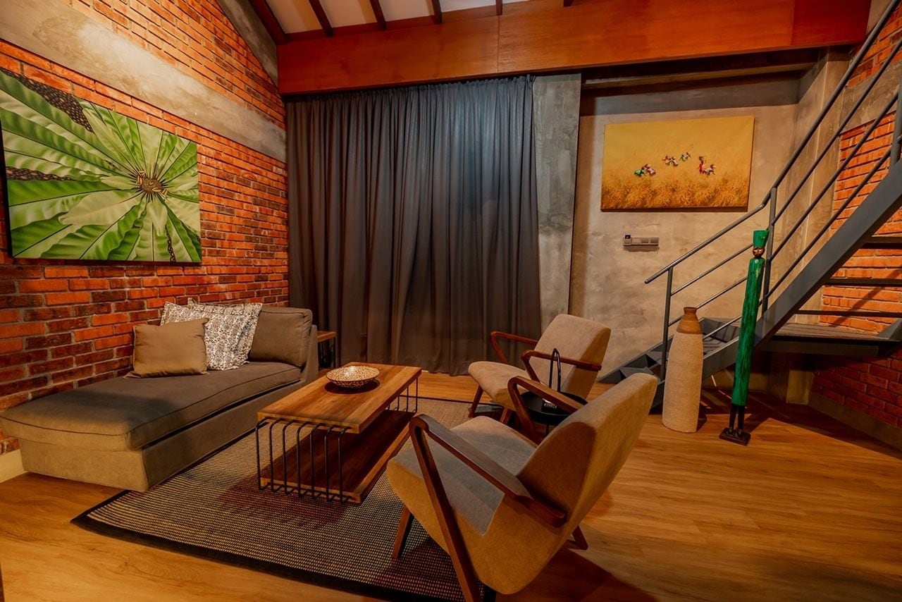 Una sala de estar acogedora con una pared de ladrillo, un cuadro abstracto verde grande, un sofá, una mesa de centro y una escalera con un jarrón verde.