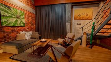 Una sala de estar acogedora con una pared de ladrillo, un cuadro abstracto verde grande, un sofá, una mesa de centro y una escalera con un jarrón verde.