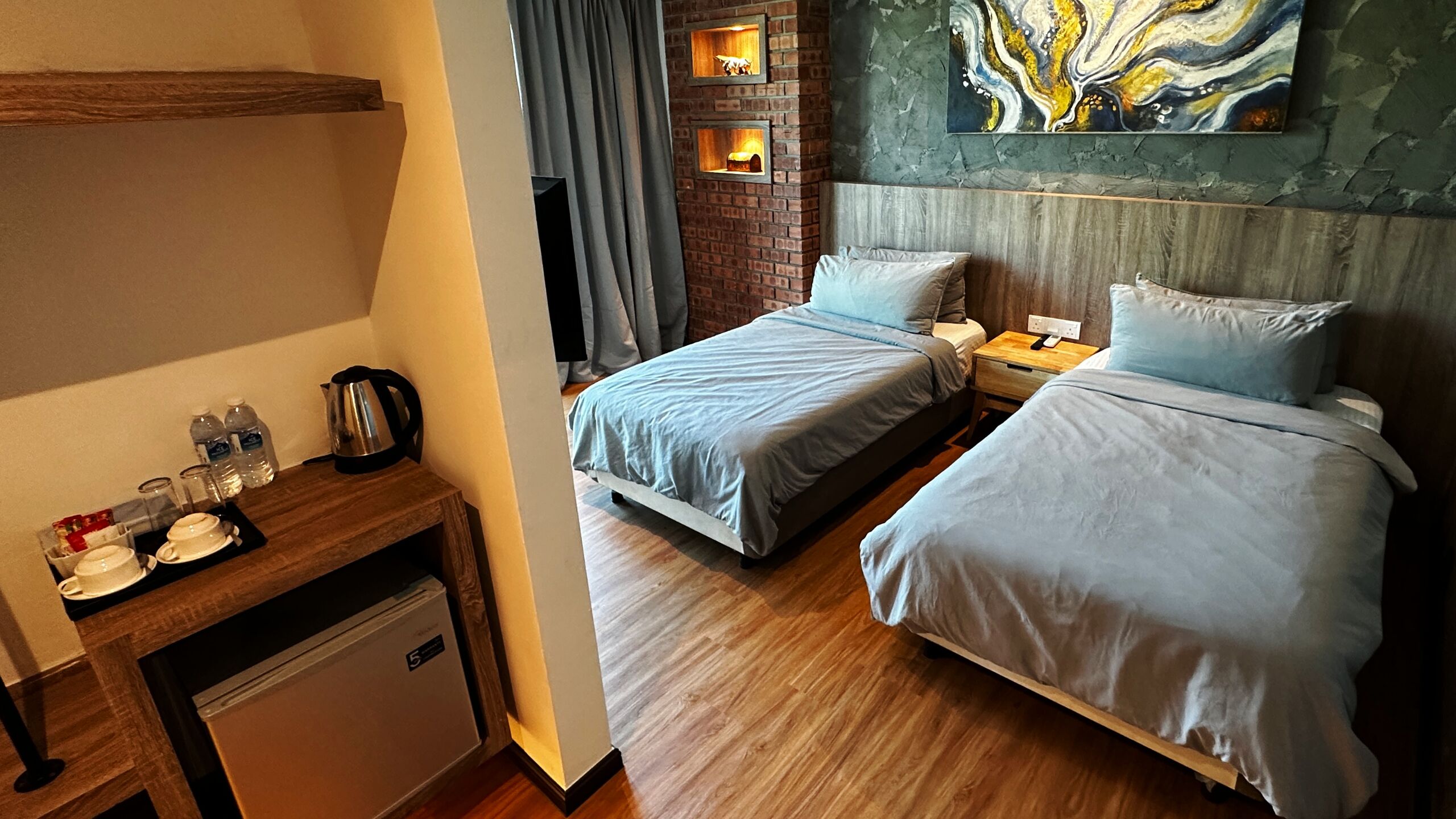 A hotel room with two beds, a small desk with a kettle, and a brick wall with a fireplace.