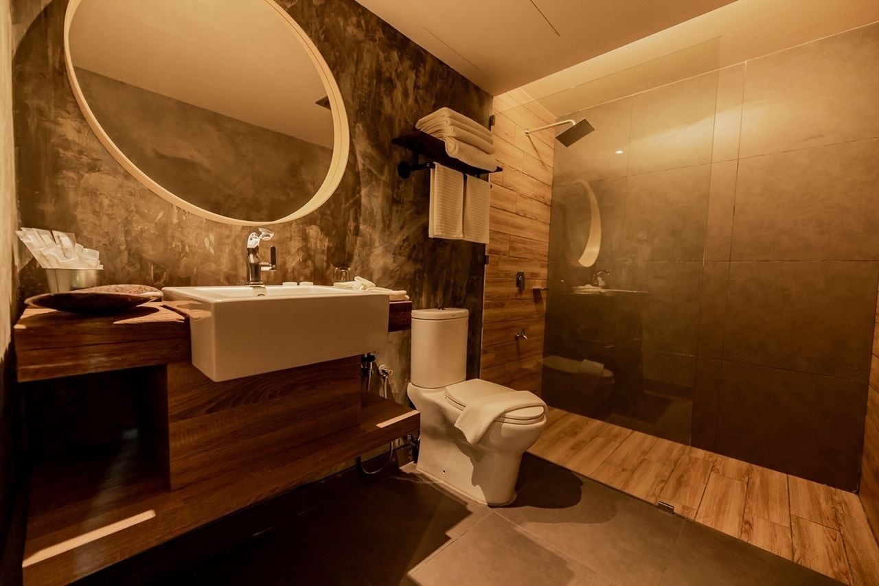 Ein modernes Badezimmer mit einem Holzbadezimmer-Möbel, einem runden Spiegel, einer Toilette und einer Duschkabine.
