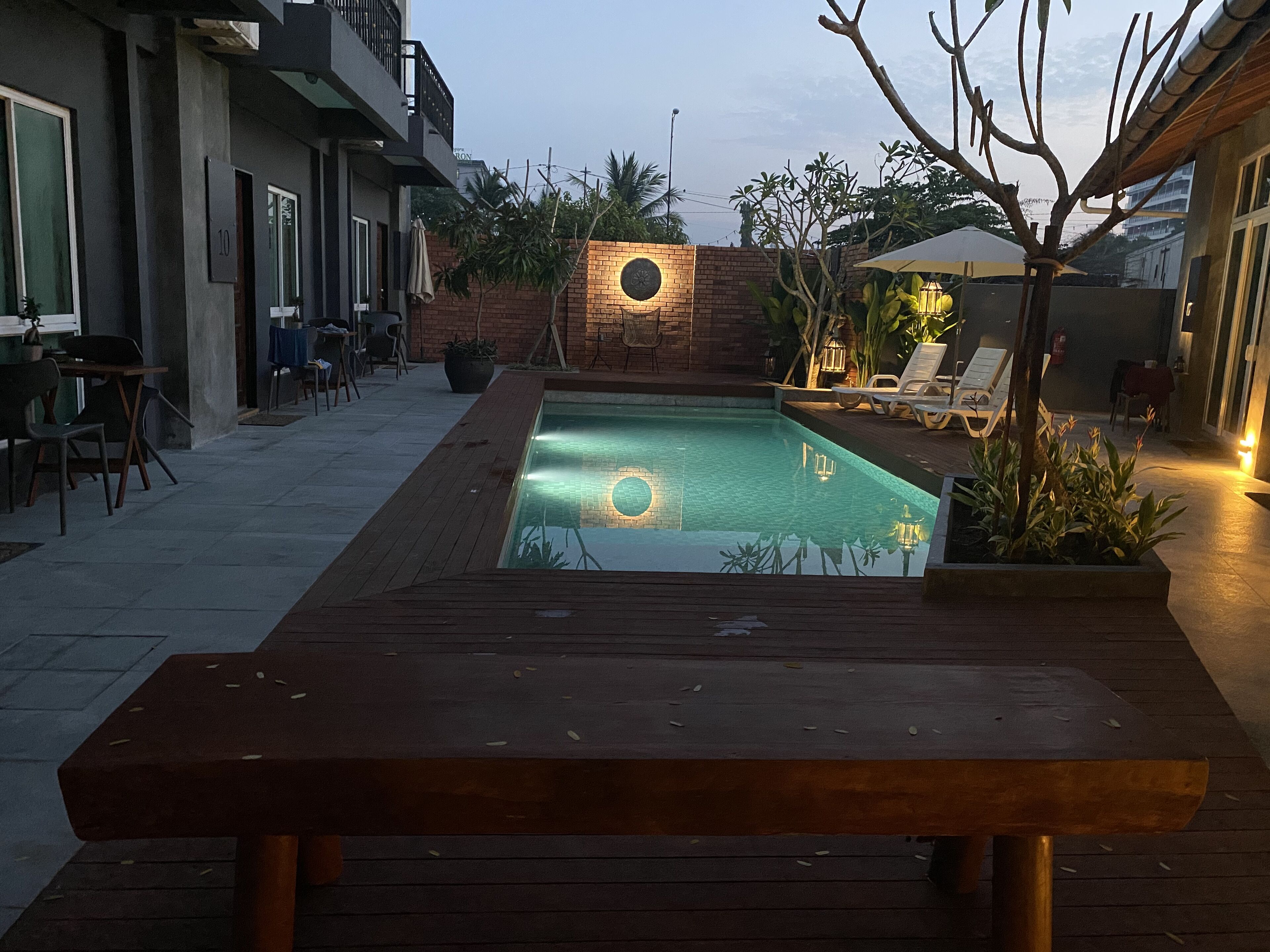 Un área de piscina con cubierta de madera, pared de ladrillo con ventanal circular y sillas de descanso.