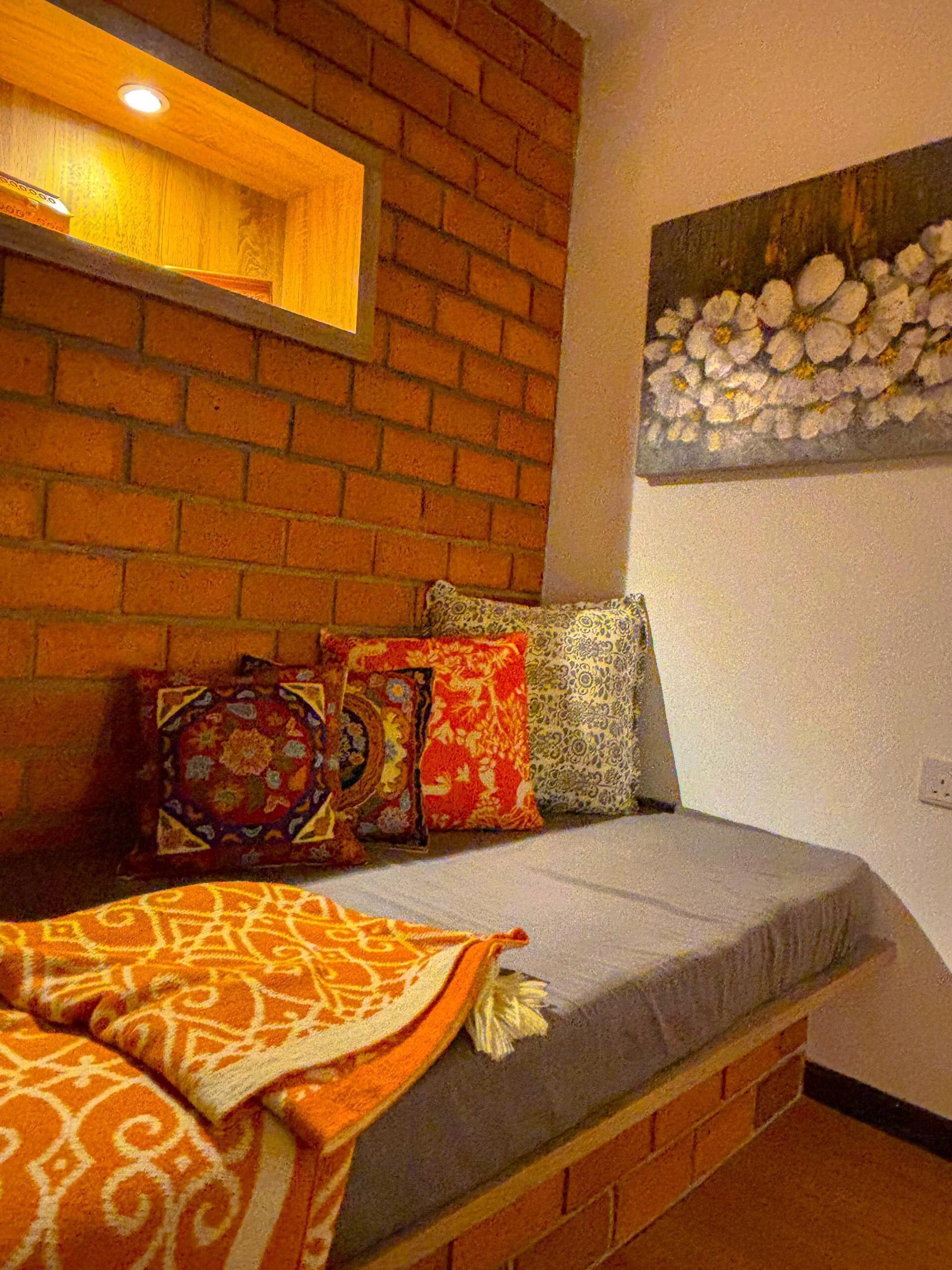 A cozy room with a brick wall, a cushioned bench, and a floral painting.