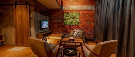 Una sala de estar moderna con pared de ladrillo, televisor de pantalla plana y un área de estar confortable con sofás y sillones.