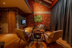 A modern living room with a brick wall, a flat-screen TV, and a comfortable seating area with sofas and chairs.