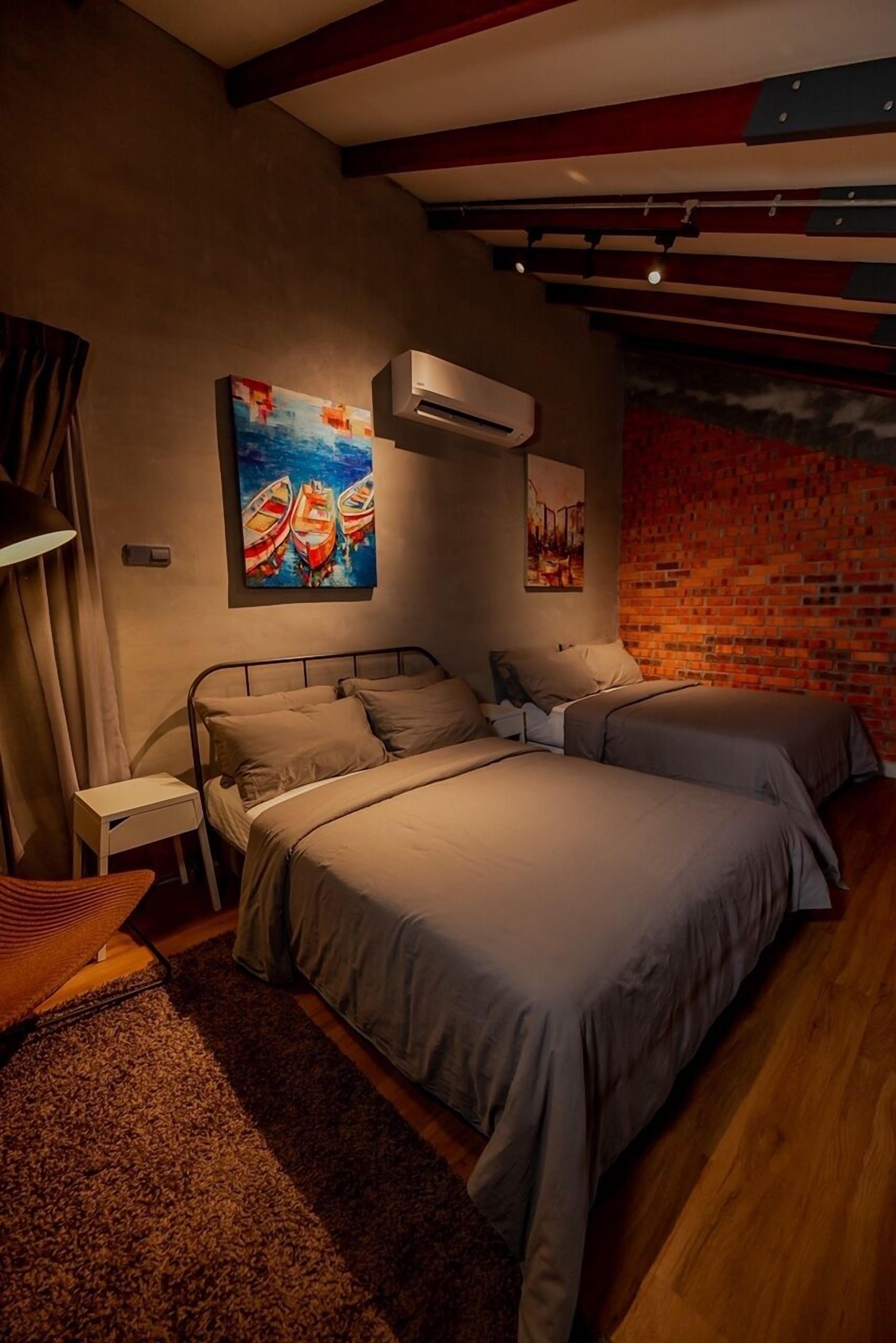 A bedroom with two beds, a brick wall, and artwork on the wall.
