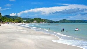 A beach with clear waters, people swimming, and a few boats. - Arch Studio Cenang (Langkawi)