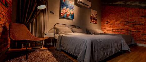 Un dormitorio con pared de ladrillo, cama con ropa de cama gris, una silla y una obra de arte en la pared.
