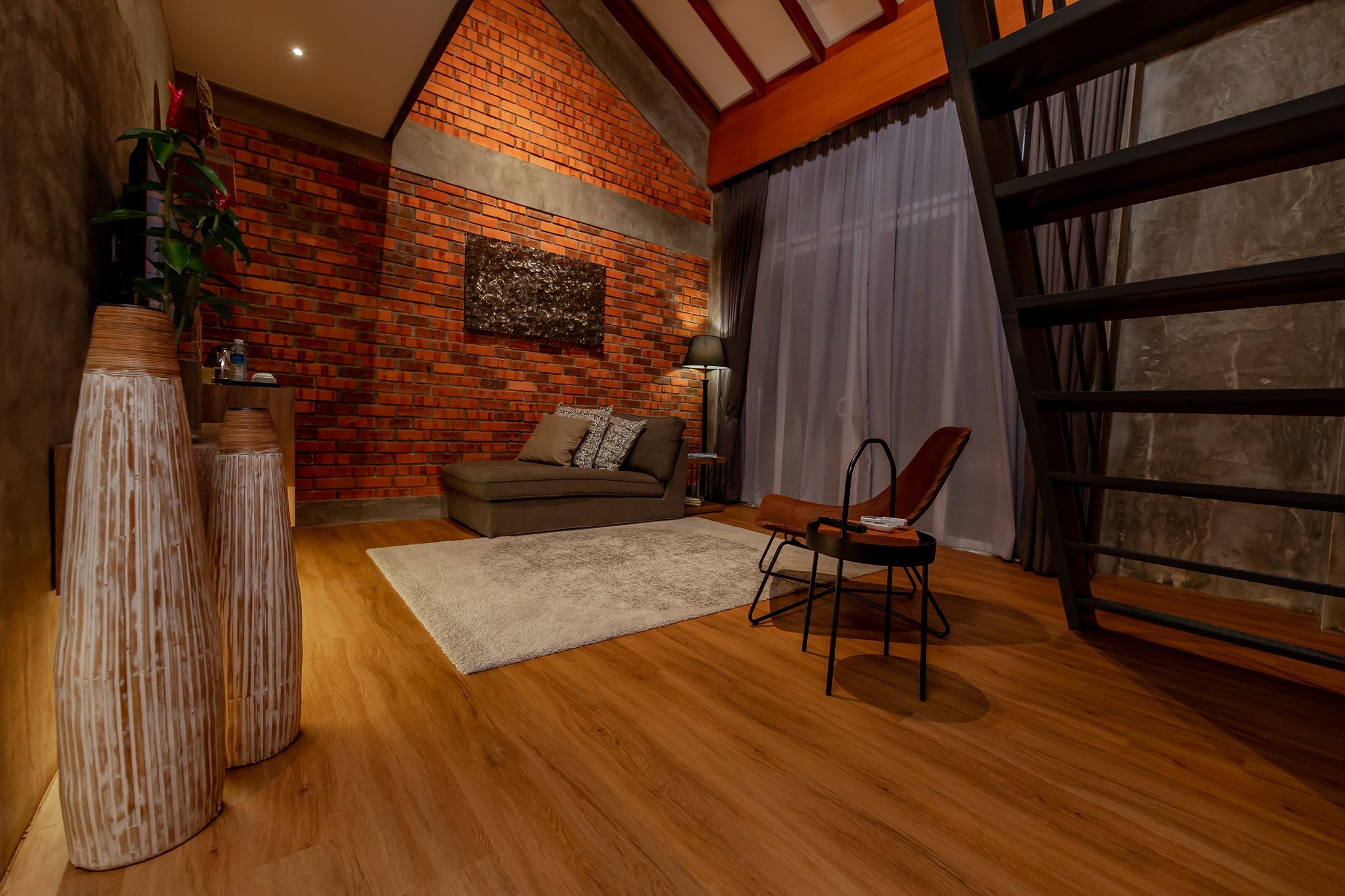 A cozy room with a brick wall, a sofa, a chair, and a large window with curtains.