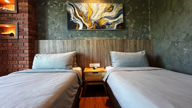 A room with two beds, a wooden headboard, a brick wall, and a large abstract painting. - Arch Studio Cenang (Langkawi)