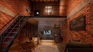 A loft-style living area with exposed brick walls, a staircase, a sofa, a coffee table, and a television. - Arch Studio Cenang (Langkawi)