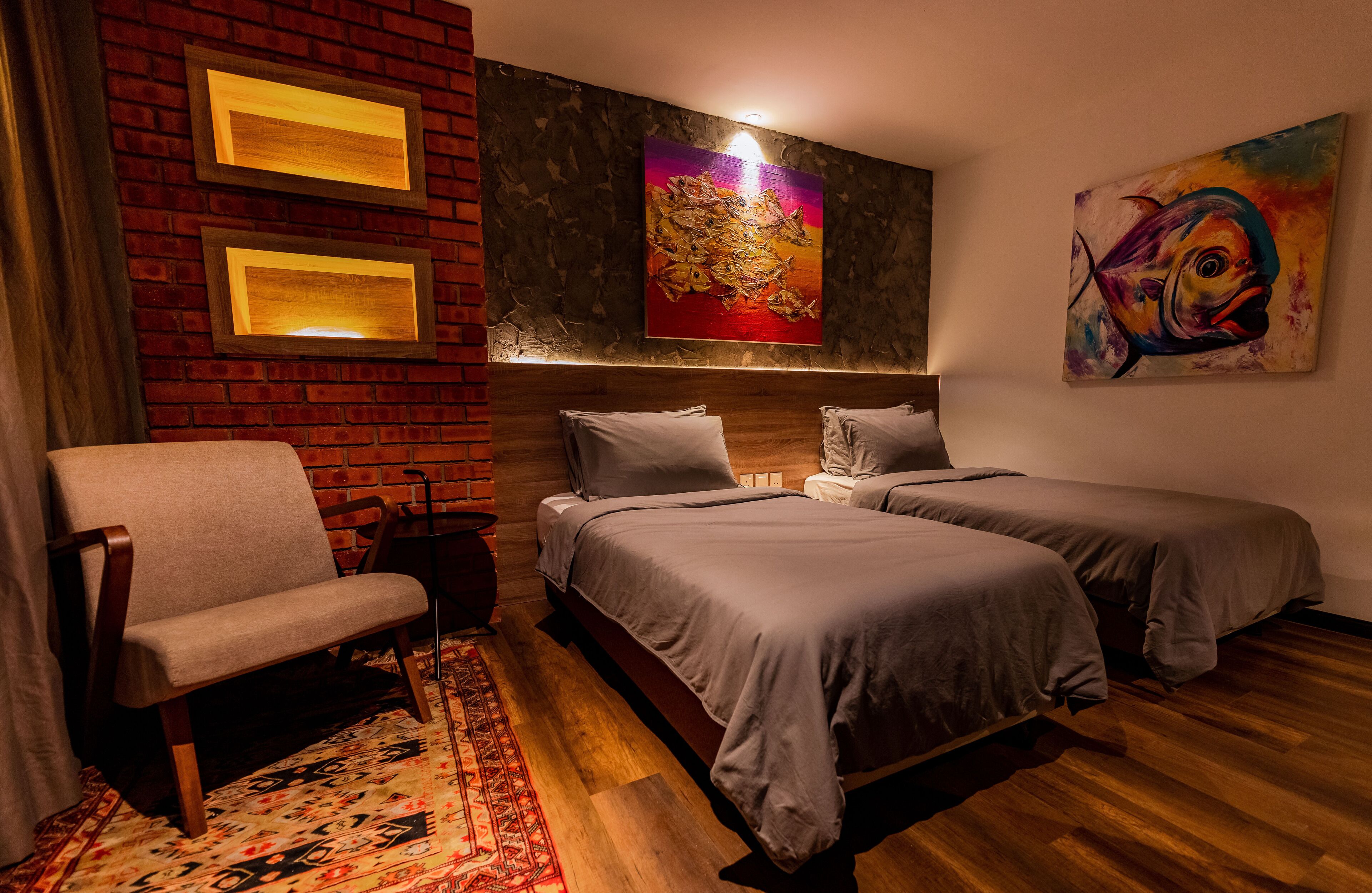 Habitación de hotel con pared de ladrillo, dos camas, una silla y obras de arte.