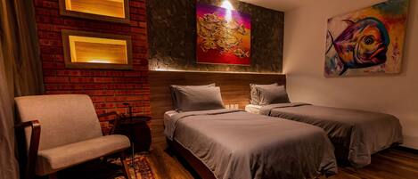 A hotel room with a brick wall, two beds, a chair, and artwork.