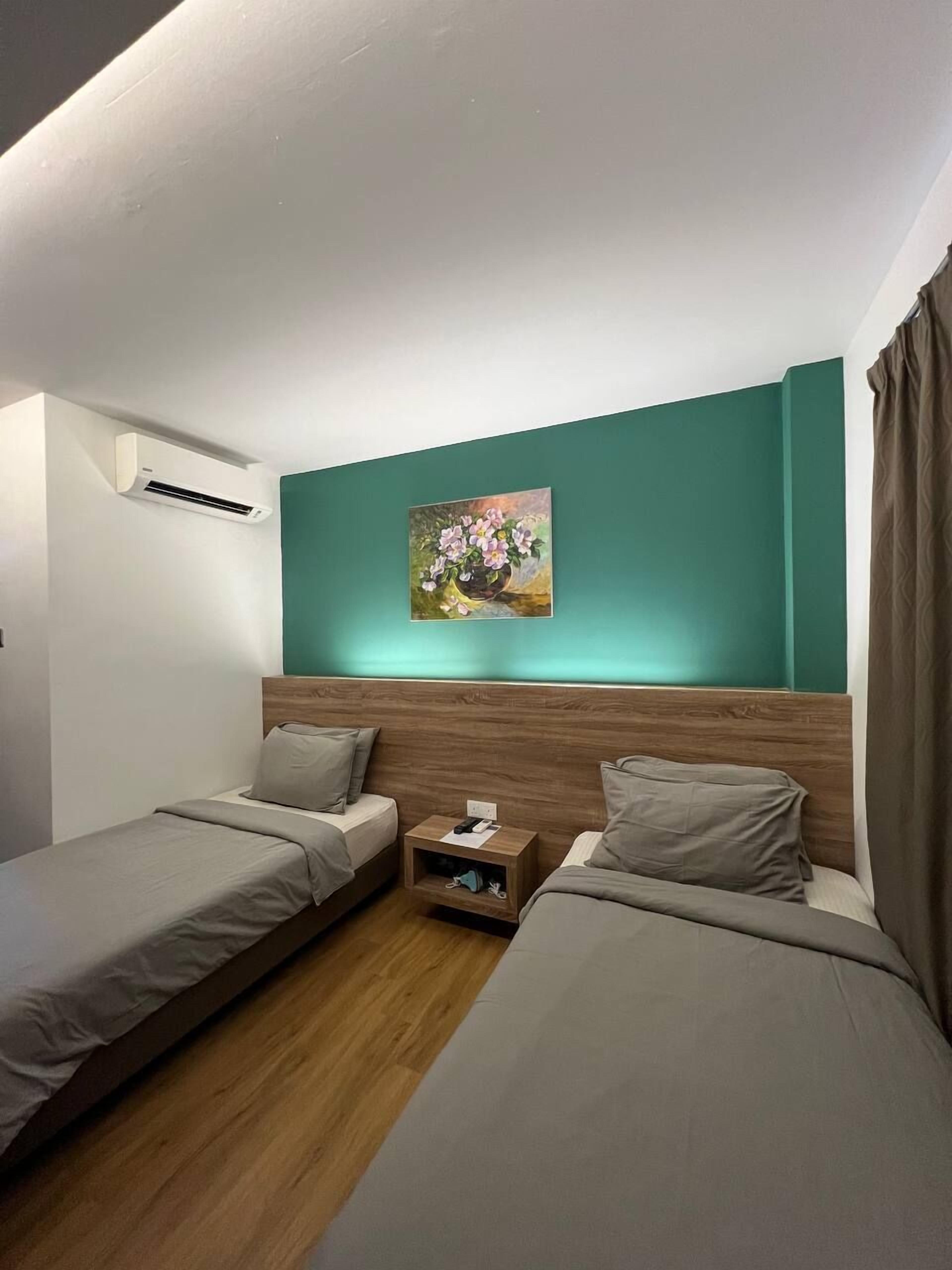 A hotel room with two single beds, a wooden headboard, a small bedside table, and a painting on the wall.